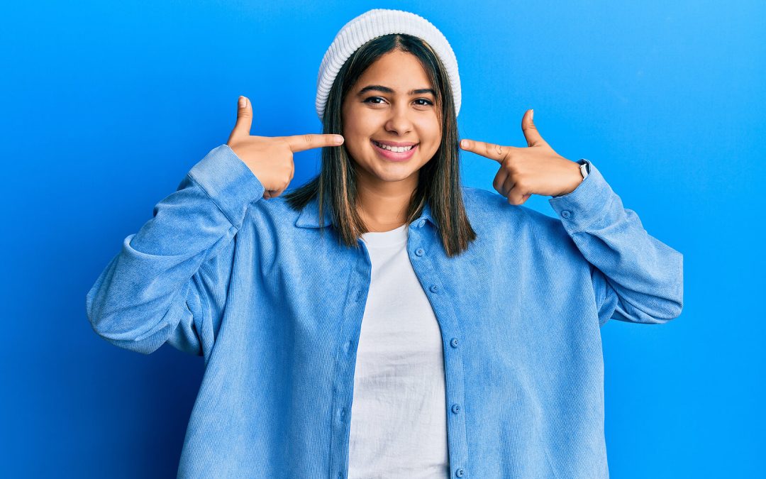 smiling woman wearing blue pointing to her teeth