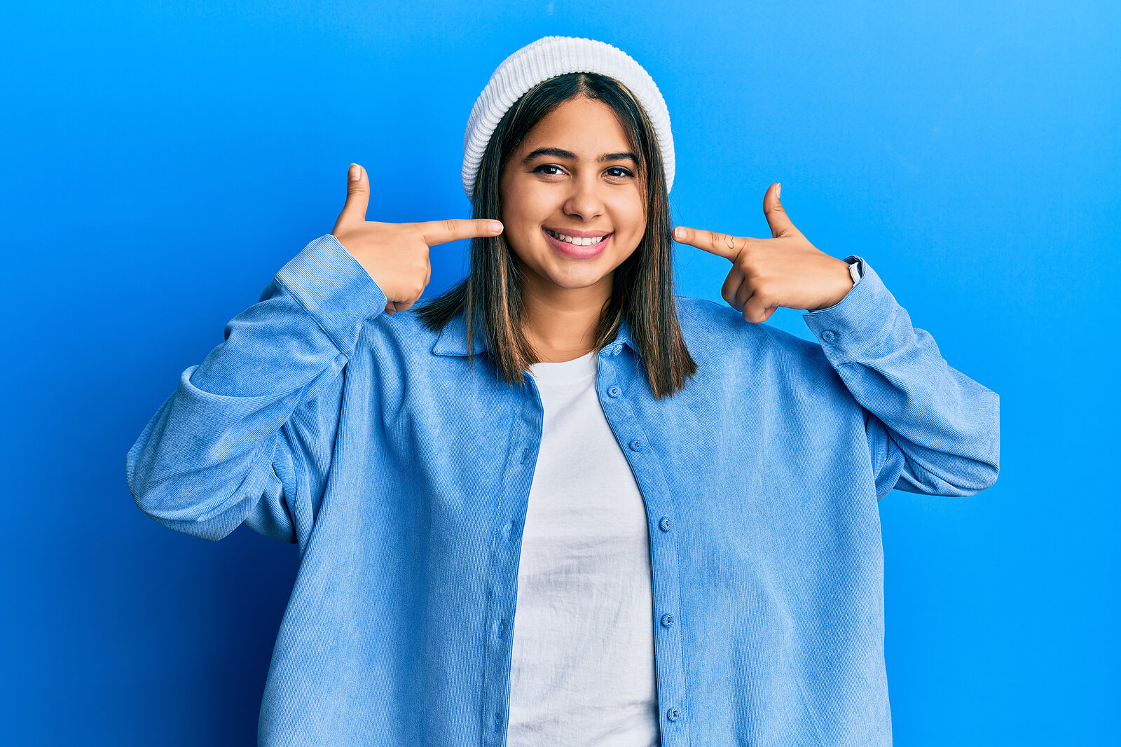 smiling woman wearing blue pointing to her teeth