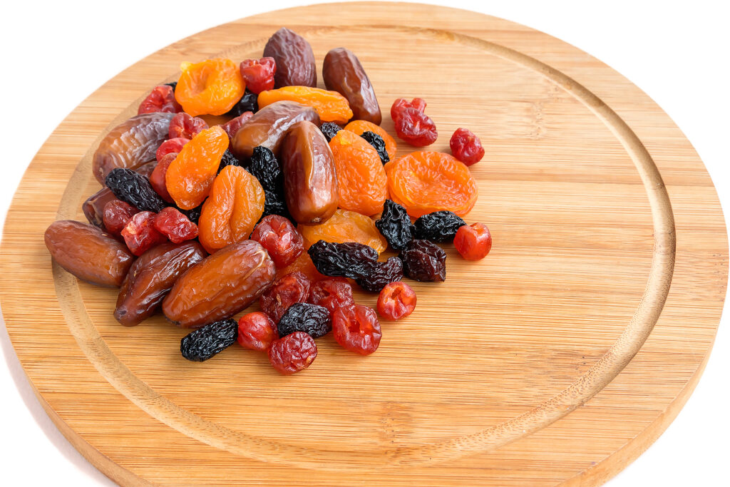 On a wooden kitchen board, a mixture of healthy tasty dried fruits - dates, apricot, raisins, cherries.Isolated on a white background.